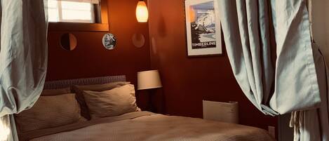 A bedroom with a bed, curtains, a lamp, a poster, and a window.