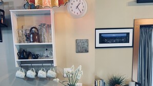 Ein Essbereich mit einem Holztisch, vier Tischsets, einer Topfpflanze und einer Uhr an der Wand.