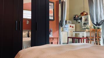 A bedroom with a bed, a wardrobe, a desk, and a kitchenette.