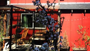 Ein rotes Gebäude mit einer überdachten Terrasse, einer Holzbank und einem Blumentopf mit weißen Blüten.