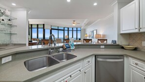 A modern kitchen with a double sink, white cabinetry, and a view of the ocean through large windows. - Phoenix West 2205 by Liquid Life (Orange Beach)