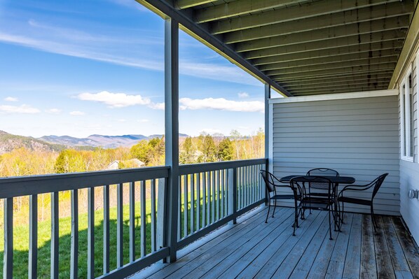 Une véranda abritée, dotée d’une table et de chaises, qui offre une vue imprenable sur un paysage magnifique, avec des montagnes et des arbres.