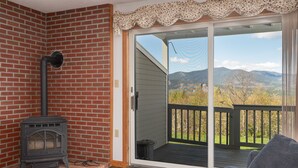 A brick fireplace with a chimney, a sliding glass door to a deck, and a view of mountains.