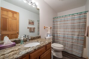 Une salle de bain avec un lavabo en marbre, des meubles en bois, des toilettes et un rideau de douche à rayures.