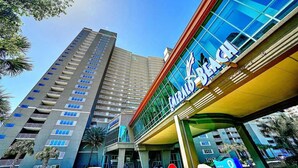 Un hotel de diseño moderno, con un llamativo letrero que dice 'Emerald Beach' y un edificio alto al fondo.