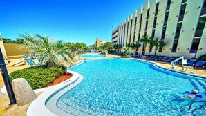 Una piscina de borde curvo, rodeada de palmeras y sillas de descanso.