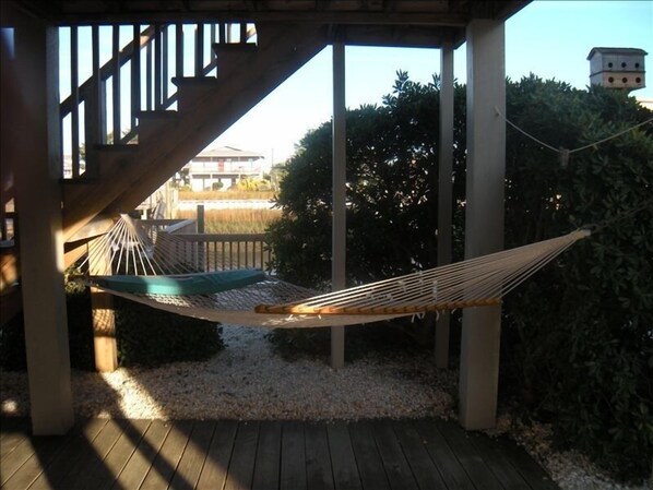 A hammock under a wooden pergola with a view of a building and trees.