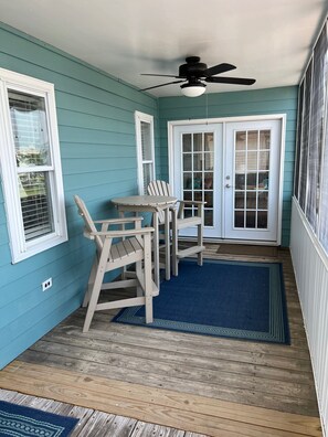A covered porch with a table and chairs, a ceiling fan, and a door with glass panels.