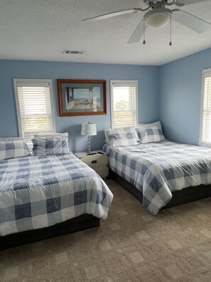 A bedroom with two beds, a ceiling fan, and a framed picture on the wall.