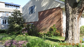 A two-story house with a brick garage, surrounded by a well-maintained garden with various plants and flowers. - Only 1.5 Blocks To Ocean, 1-3 blocks of restaurants, shops, bars. Come enjoy! (Rehoboth Beach)