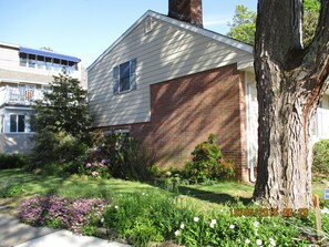 A two-story house with a brick garage, surrounded by a well-maintained garden with various plants and flowers.