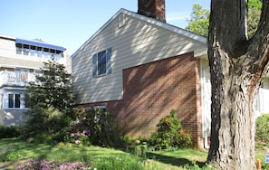 A two-story house with a brick garage, surrounded by a well-maintained garden with various plants and flowers.