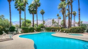 A swimming pool with lounge chairs, surrounded by palm trees and mountains in the background. - South Palm Springs Condo - Fantastic Mountain Views! (Palm Springs)