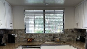 A modern kitchen with white cabinets, a stainless steel dishwasher, a granite countertop, and a window with blinds. - South Palm Springs Condo - Fantastic Mountain Views! (Palm Springs)