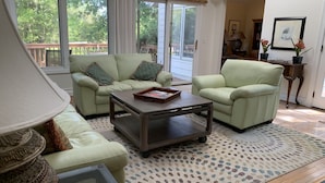 A living room with two green sofas, a coffee table, a patterned rug, and a view of the outdoors through large windows. - Private End Of Street - Home In Lawton Woods (Hilton Head Island)