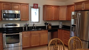 A modern kitchen with wooden cabinets, stainless steel appliances, and a dining area with a wooden table and chairs. - Private End Of Street - Home In Lawton Woods (Hilton Head Island)