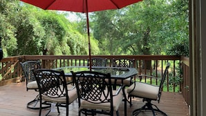 A wooden deck with a round table and chairs, a red umbrella, and a view of lush greenery. - Private End Of Street - Home In Lawton Woods (Hilton Head Island)