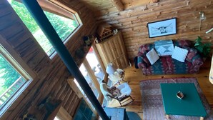Interior rústico de una cabaña con paredes de madera, un sofá verde, una mesa de comedor y un lámpara colgante.