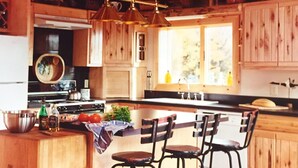 Una cocina rústica con armarios de madera, una isla central con taburetes de bar y una lámpara colgante.