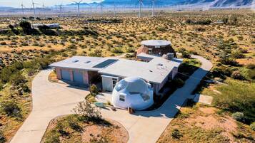 A modern building with a unique spherical structure, surrounded by a desert landscape and wind turbines in the background.