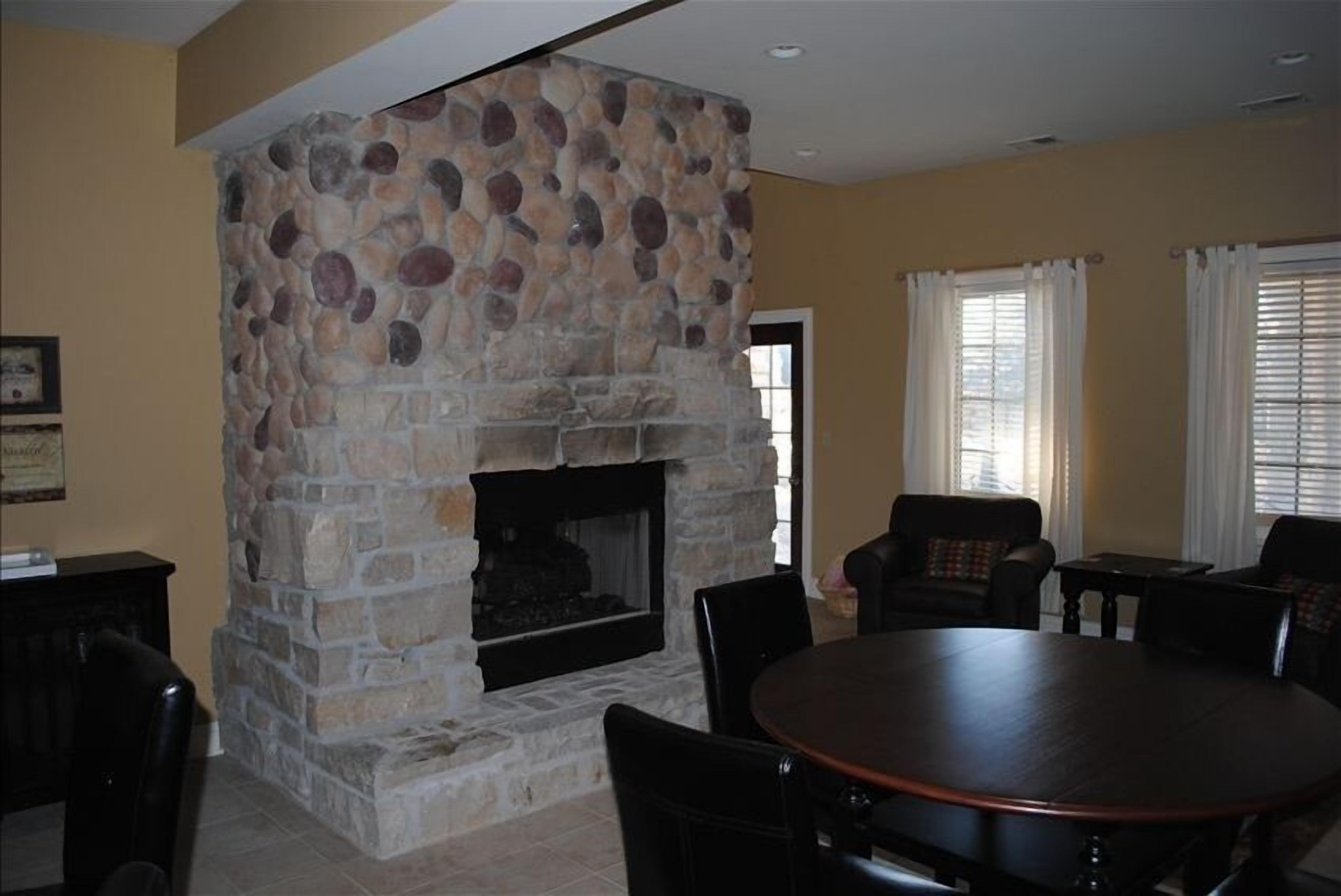 A stone fireplace with a fire, surrounded by a dining area with chairs and a table.
