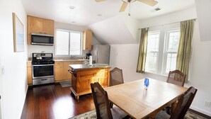 A kitchen with wooden cabinets, a microwave, a stove, and a refrigerator. There is a dining table with chairs and a window with curtains. - Charming 1870 Farmhouse in the Heart of Petaluma
 (Petaluma)