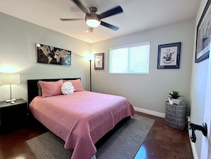 Un dormitorio con una cama, un ventilador de techo, un mapa del mundo y cuadros en la pared.