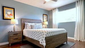 Ein Schlafzimmer mit einem hölzernen Bett, zwei Nachttischen mit Lampen, einem Deckenventilator und gerahmten Kunstwerken an den Wänden.