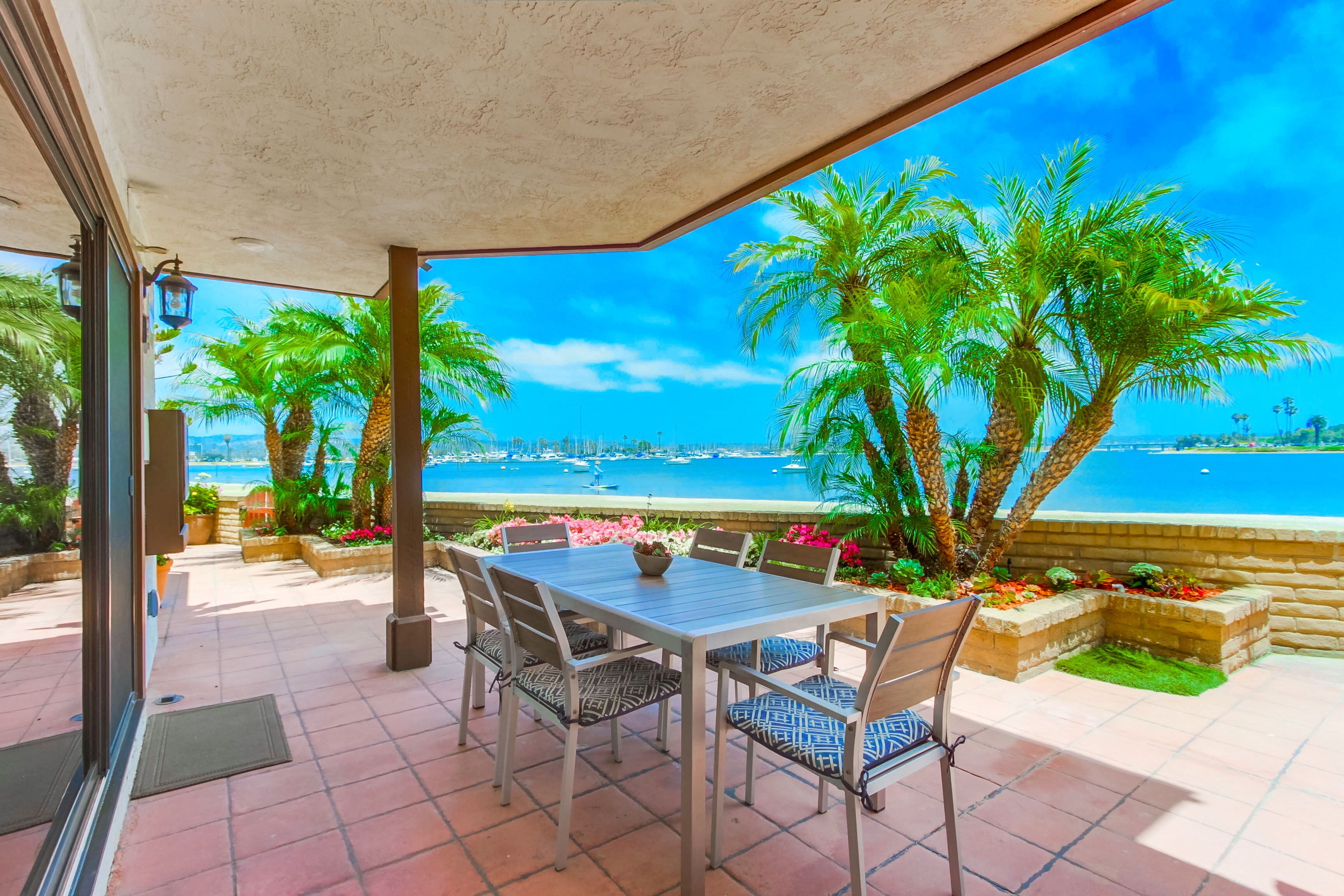 Une terrasse extérieure avec une table et des chaises, des palmiers et une vue sur la mer.