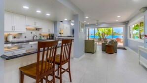 Una cocina moderna con armarios blancos, un comedor con sillas de madera y vistas al océano a través de amplios ventanales.