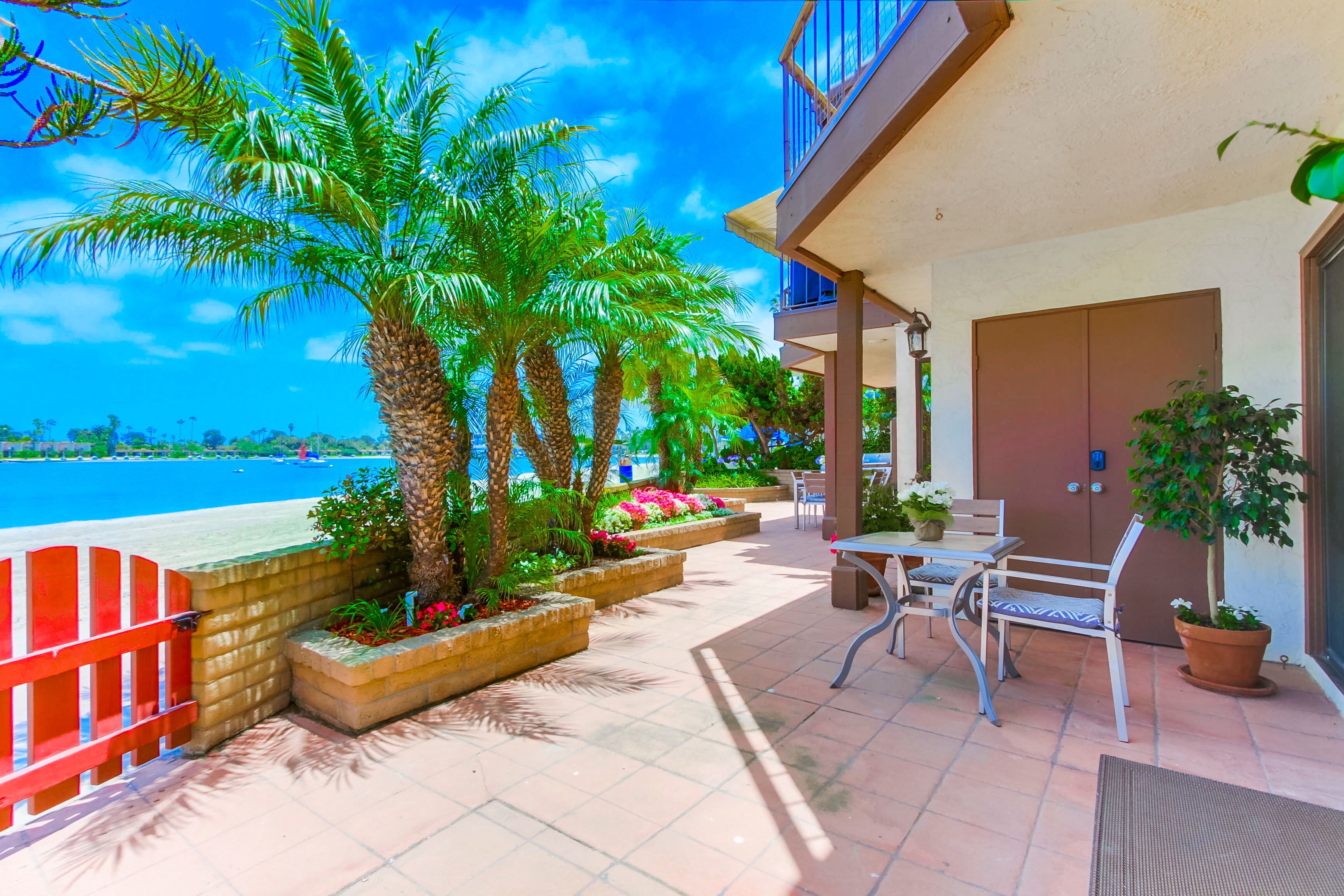 A balcony with a view of the sea, palm trees, and a seating area with a table and chairs.
