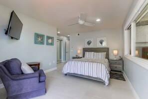 A bedroom with a bed, a chair, a TV, and artwork on the walls.