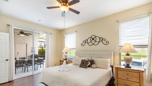 A bedroom with a large bed, a ceiling fan, and a nightstand with a lamp.
