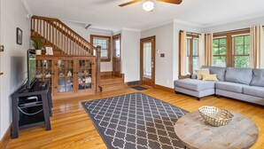 A spacious living room with hardwood floors, a gray sectional sofa, a ceiling fan, and a staircase leading to a second floor. - Walk to ND and Eddy Street, ProCleaned * Comfy * Updated (South Bend)