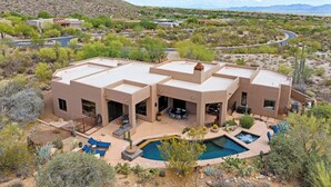 Une maison moderne avec une piscine, entourée de végétation désertique et de montagnes.