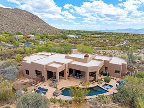 Una casa moderna con piscina, rodeada de vegetación desértica y montañas.