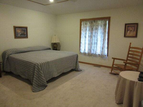 A bedroom with a bed, a chair, a lamp, and a window with curtains. - Spacious Home, Awesome View, Close to Lakes, Comfortably Sleeps 18 People (Holiday Island)