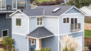 A two-story house with a gabled roof, a front porch, and a landscaped garden with various plants and a small water feature. - Coastal View Home - Newly Remodeled.  Water Taxi Ride Away to see the WORLD CUP! (Seattle)