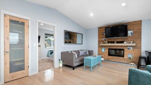 A modern living room with a grey sofa, a blue coffee table, and a TV mounted on a wooden wall. - Coastal View Home - Newly Remodeled.  Water Taxi Ride Away to see the WORLD CUP! (Seattle)