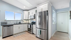 A modern kitchen with white cabinets, stainless steel appliances, and a large window. - Coastal View Home - Newly Remodeled.  Water Taxi Ride Away to see the WORLD CUP! (Seattle)