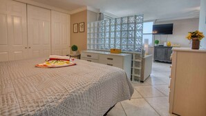 Quarto com uma cama grande, cômoda, penteadeira, janela com vista e televisão fixada na parede.