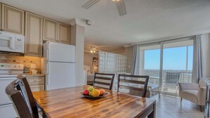 Cozinha moderna com eletrodomésticos brancos, uma mesa de jantar de madeira com frutas e uma varanda com vista.