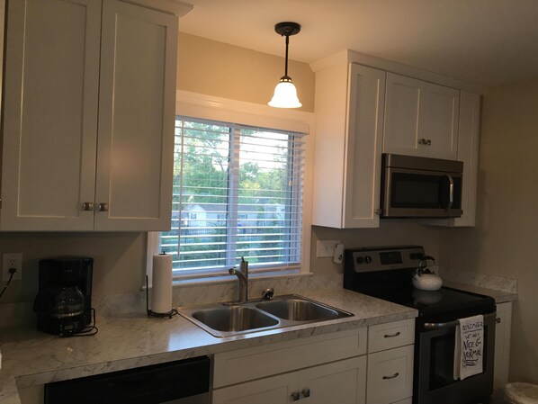 A kitchen with white cabinets, a stainless steel sink, a microwave, and a window with blinds.
