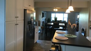 Una cocina moderna con un refrigerador de acero inoxidable empotrado, una zona de comedor con una mesa y sillas de madera oscura, e iluminación colgante.