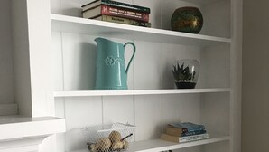 Una estantería blanca con libros, objetos decorativos y un jarrón con flores.