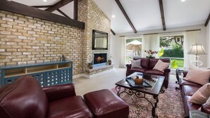 A spacious living room with a stone fireplace, leather furniture, and large windows offering a view of the outdoors.