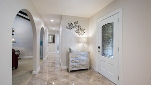 A hallway with a marble floor, a white door with a glass panel, and a wall-mounted decorative piece.