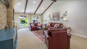 A spacious living room with a fireplace, leather sofas, and a large window providing a view of the outdoors.