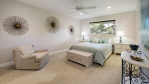 A bedroom with a bed, a chair, a bench, a ceiling fan, wall art, and a window with blinds.