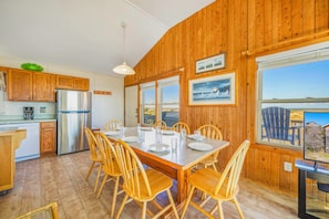 A wooden interior with a dining table set for four, kitchen cabinets, a refrigerator, and large windows offering a view. - Oceanfront Bella Beach Box - Dog Friendly w/ Hot Tub and Direct Beach Access (Avon)